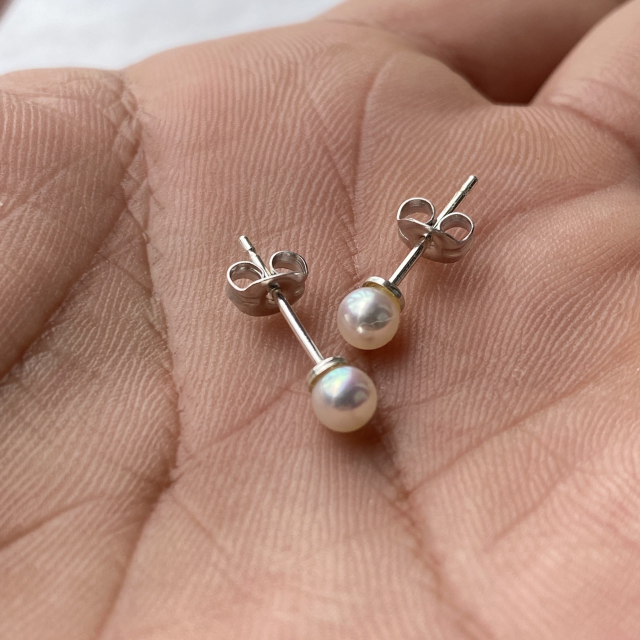 Tiny Baby Akoya pearl stud earrings in hand showing their small scale