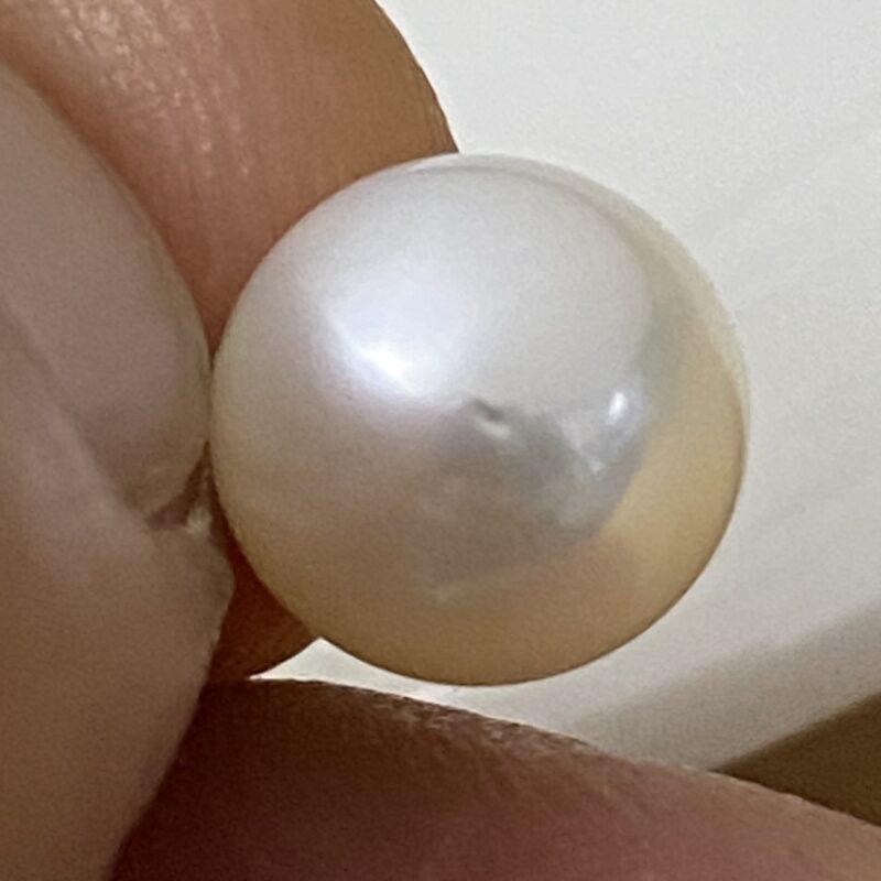 Close-up of a natural white Akoya pearl held between fingers