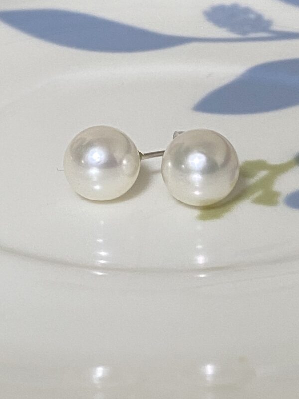 Front view of non-toned Akoya pearl earrings on a patterned dish