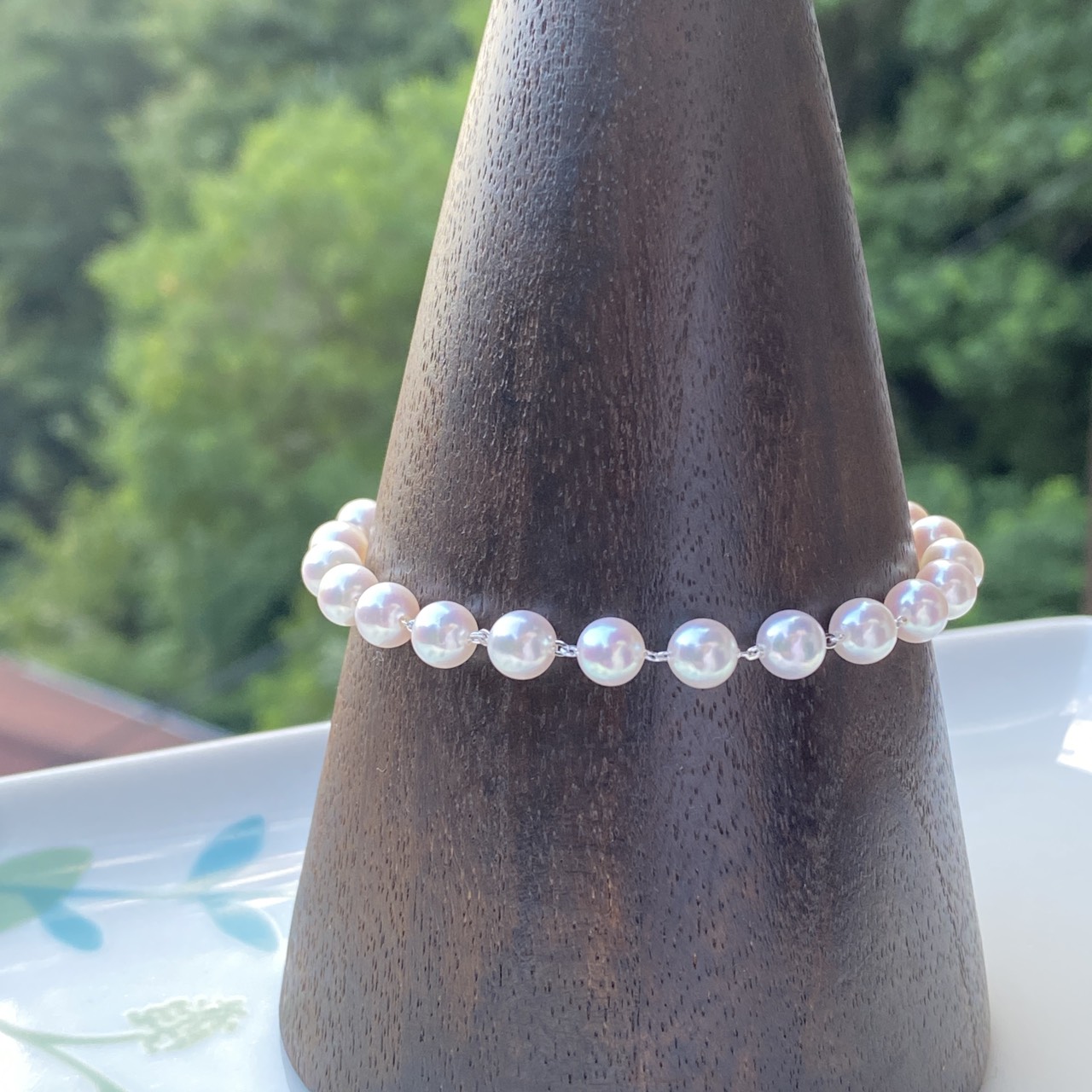 Front view of small white-pink Akoya pearls linked with sterling silver chain on a wooden display.