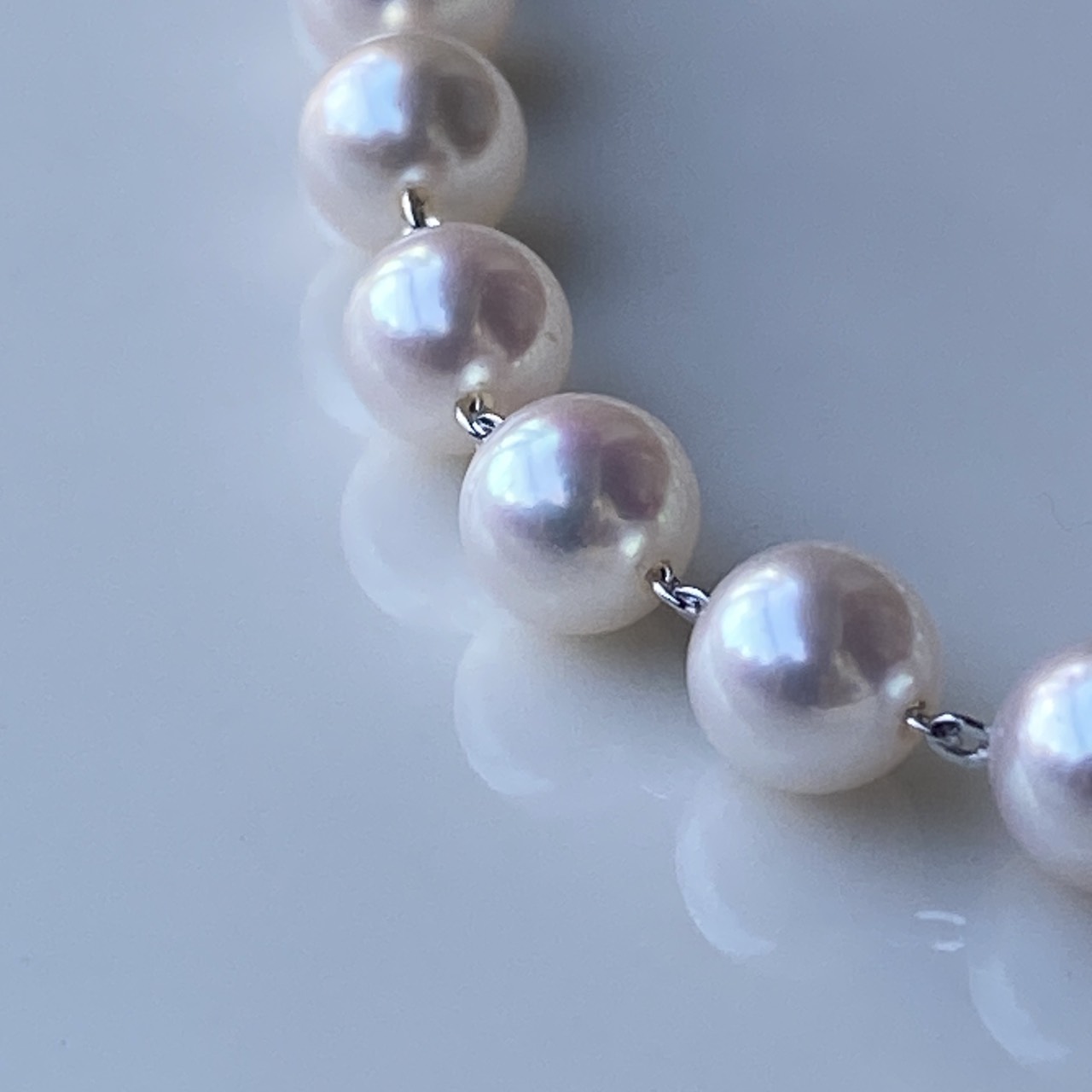 Macro close-up of round white-pink Akoya pearls and individual silver links.