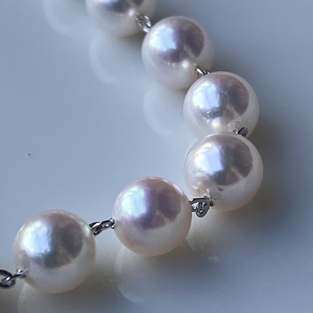 Macro detail of white-pink Akoya pearls individually connected by silver chain.